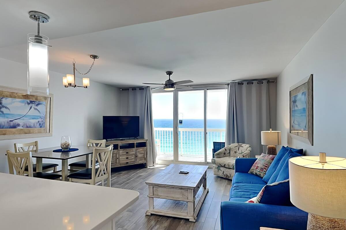A modern living room with a TV, dining area, and a balcony with a view of the ocean.