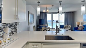 A modern kitchen with a central island, a dining area with a view, and a living space with a sofa and armchairs. - Pelican Beach by Southern Vacation Rentals (Destin)
