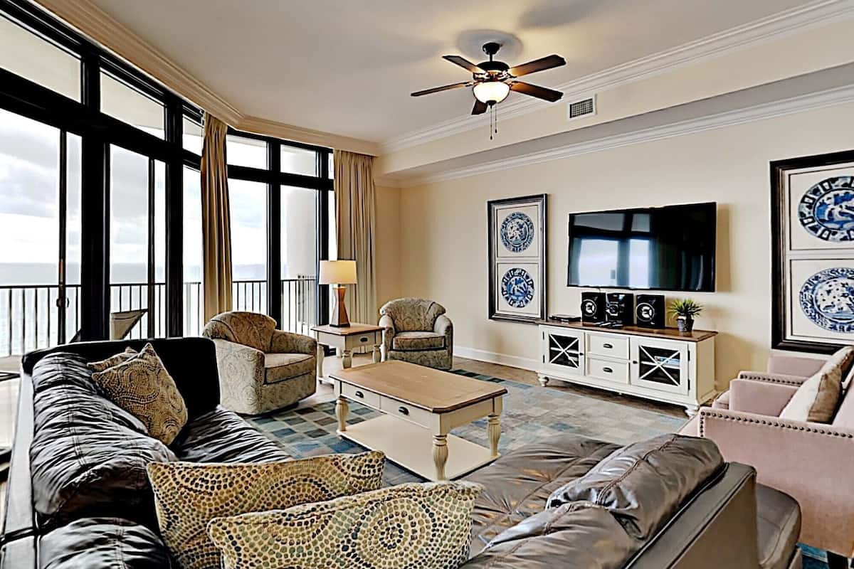 Un salon spacieux doté d’une grande fenêtre, d’un ventilateur de plafond, d’un téléviseur et d’une table basse.