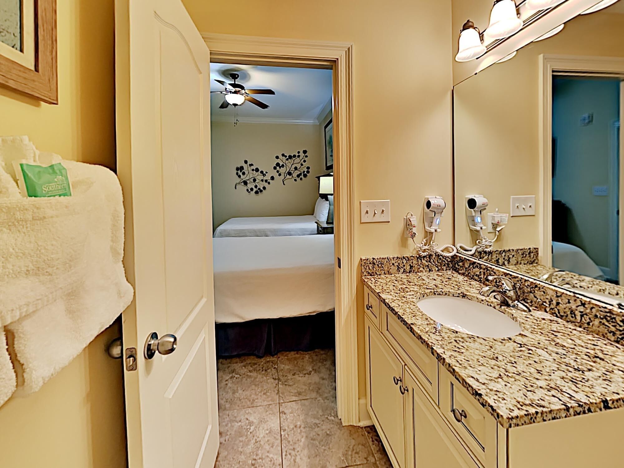 A hotel bathroom with a granite countertop, a sink, and a ceiling fan.