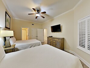 Habitación de hotel con dos camas, ventilador de techo, televisor, cómoda y ventana con persianas.