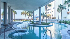 A swimming pool with a curved design, surrounded by lounge chairs and palm trees. - The Oasis at Orange Beach by Southern Vacation Rentals (Orange Beach)