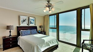 A bedroom with a large bed, a ceiling fan, and a view of the ocean through large windows. - Perdido Towers by Southern Vacation Rentals (Pensacola)