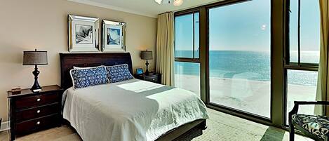 A bedroom with a large bed, a ceiling fan, and a view of the ocean through large windows.
