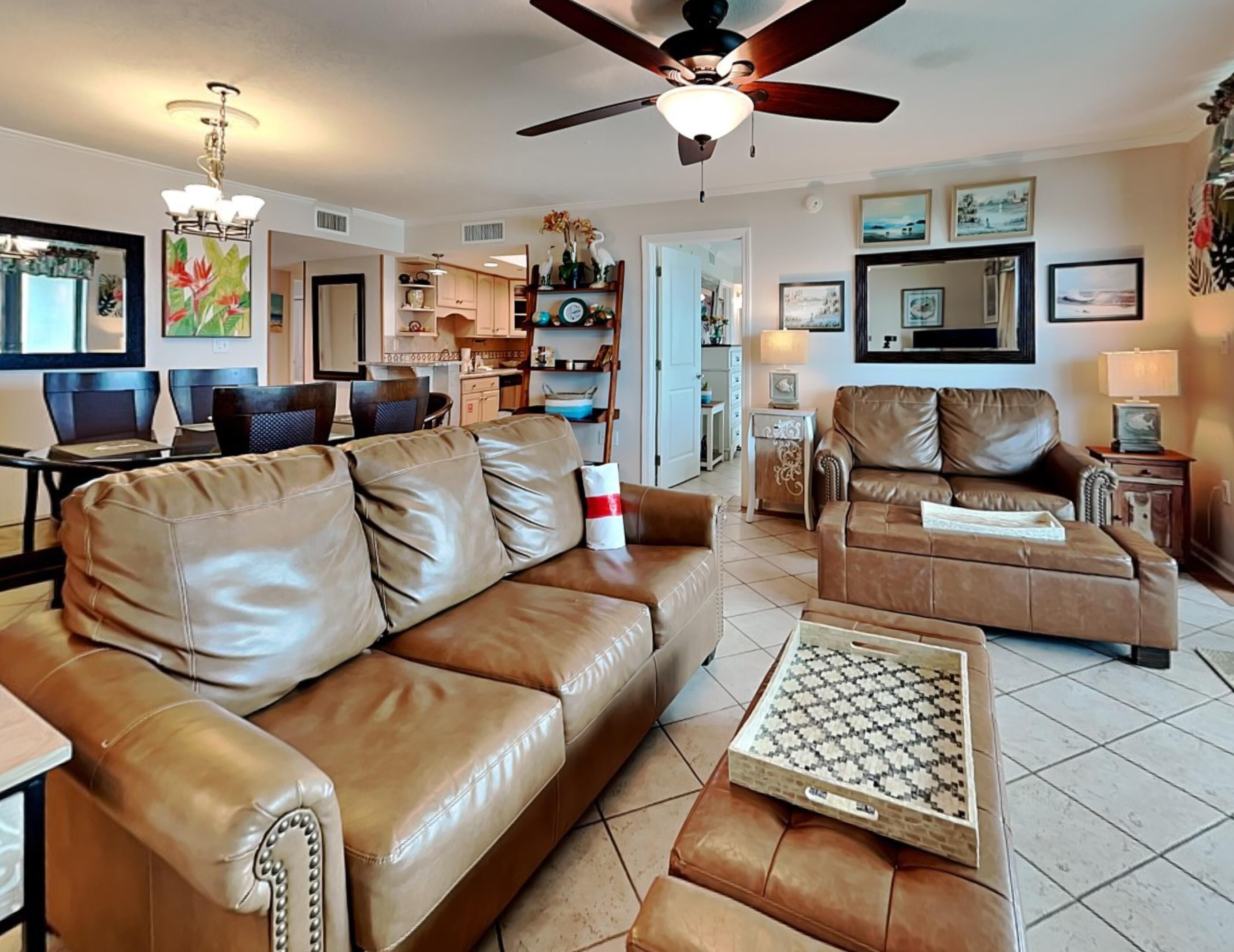 A spacious living room with leather sofas, a coffee table, and a ceiling fan.