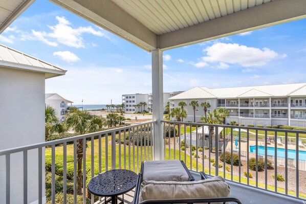 A balcony with a view of a pool, palm trees, and a building complex.