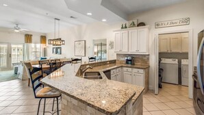 A spacious kitchen with granite countertops, white cabinetry, and a dining area with a large island. - Pavilion Palms by Southern Vacation Rentals (Miramar Beach)