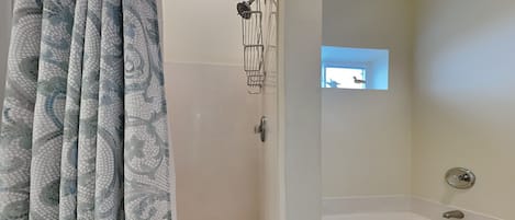 A bathroom with a shower, a bathtub, and a window with a view of the sky.