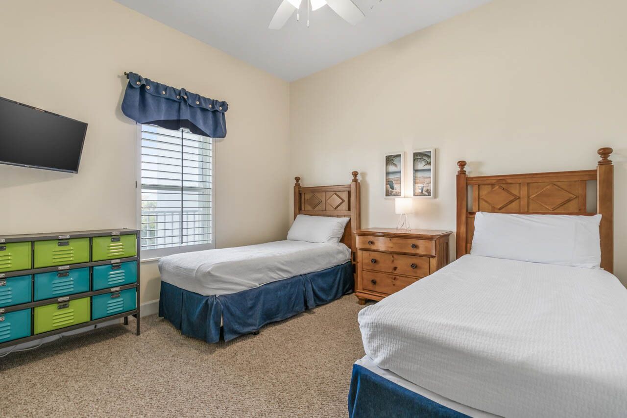 A bedroom with two beds, a TV, a dresser, and a window with blinds.