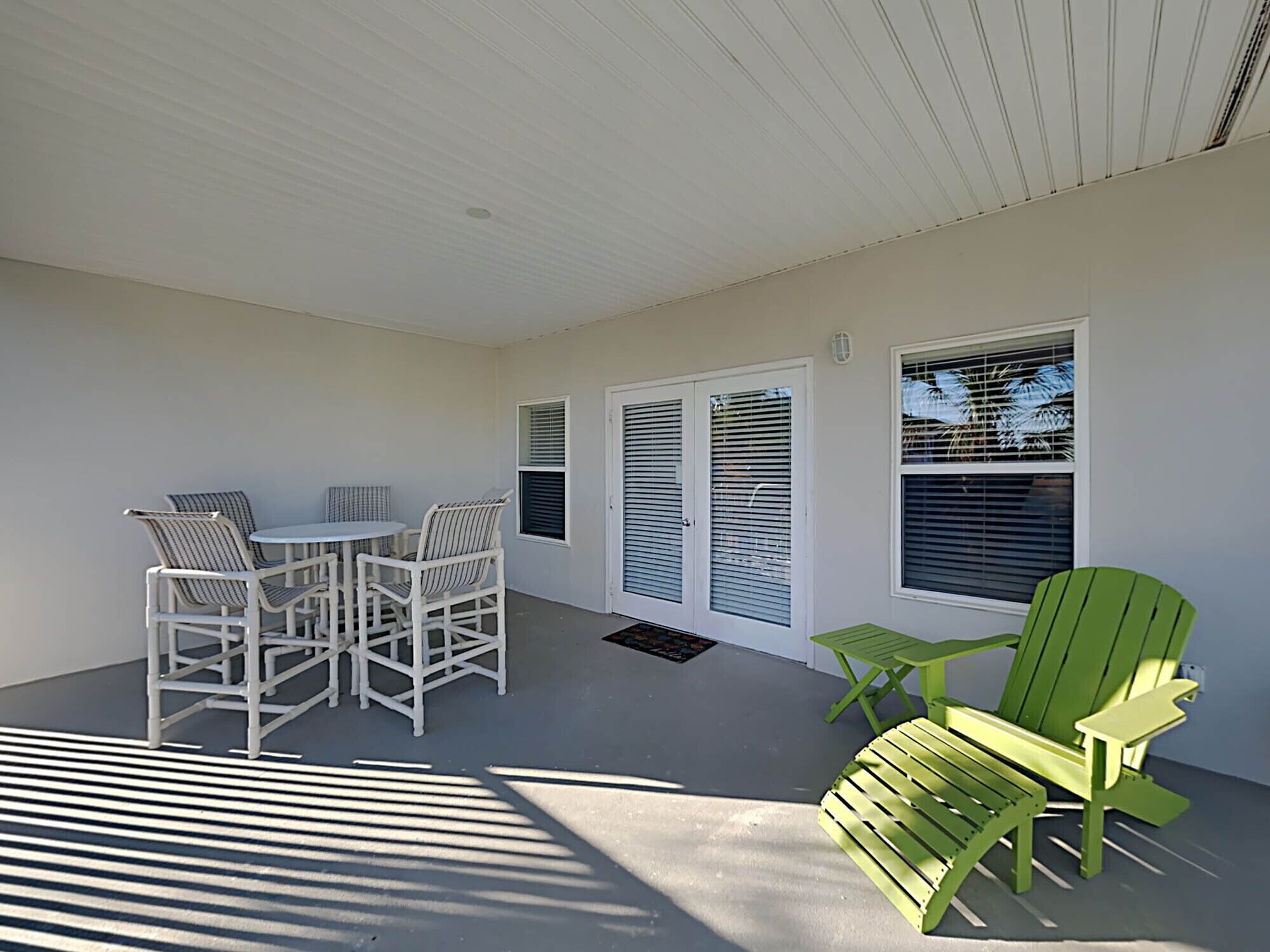 A covered patio with a table and chairs, a green Adirondack chair, and a sliding glass door.