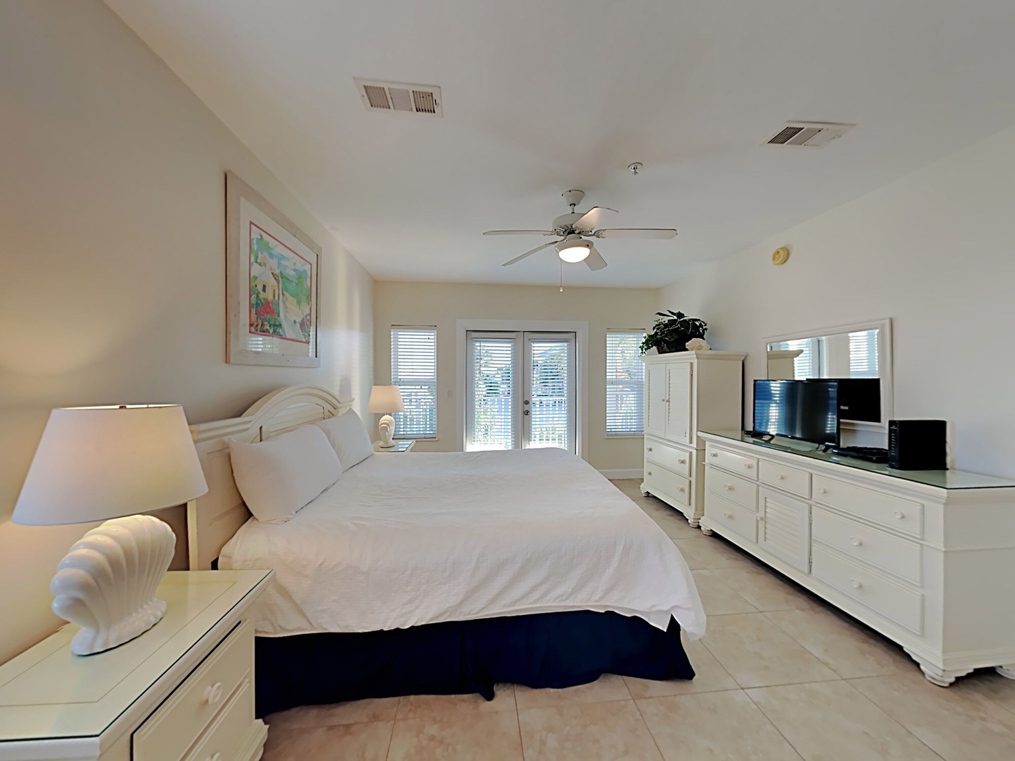 A bedroom with a bed, a nightstand, a dresser, a ceiling fan, and a TV.