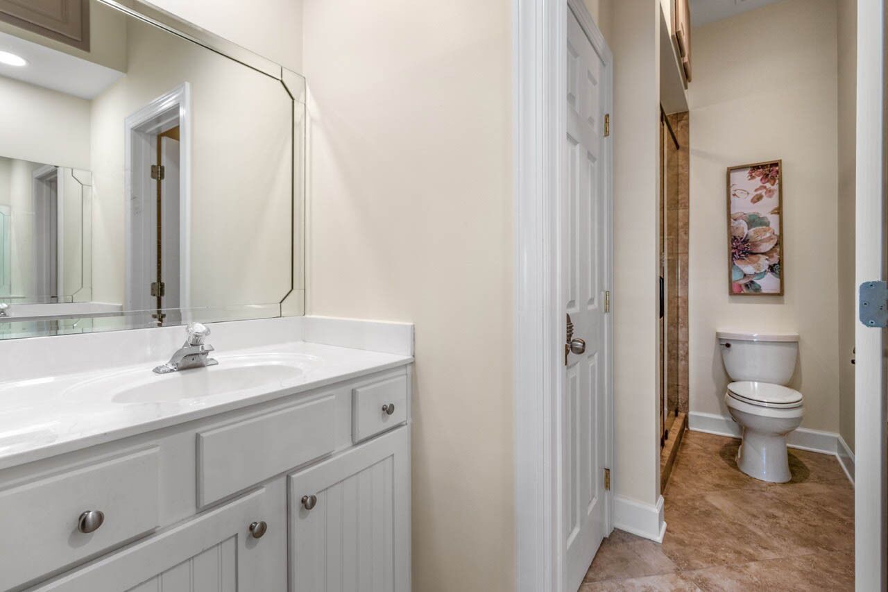 A bathroom with a white vanity, a large mirror, a toilet, and a floral artwork on the wall.
