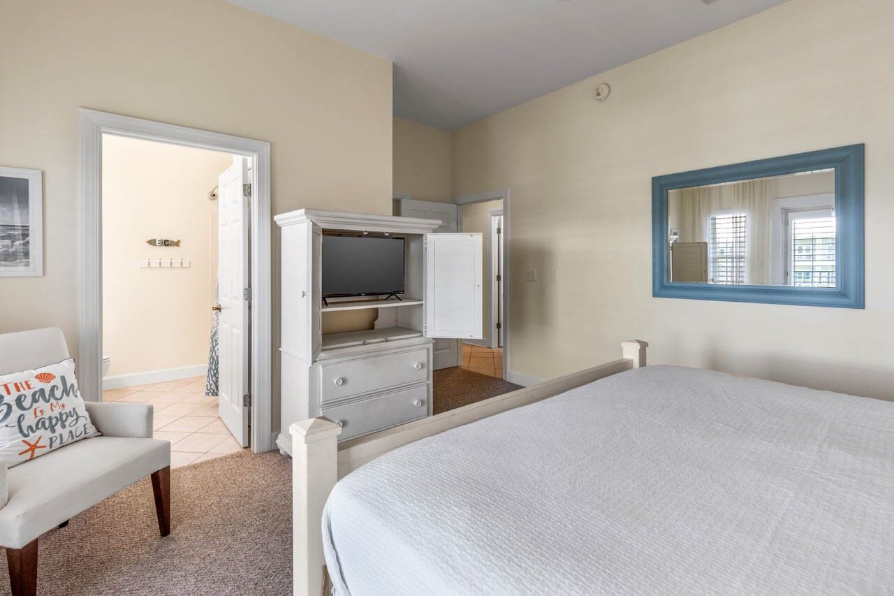 A bedroom with a bed, a dresser, a television, and a mirror.