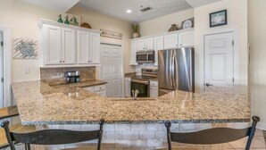 A kitchen with white cabinets, granite countertops, stainless steel appliances, and a brick accent wall. - Pavilion Palms by Southern Vacation Rentals (Miramar Beach)