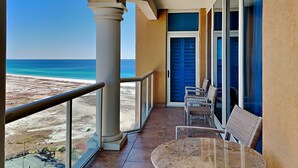 A balcony with a view of the beach, a round table, and two chairs.