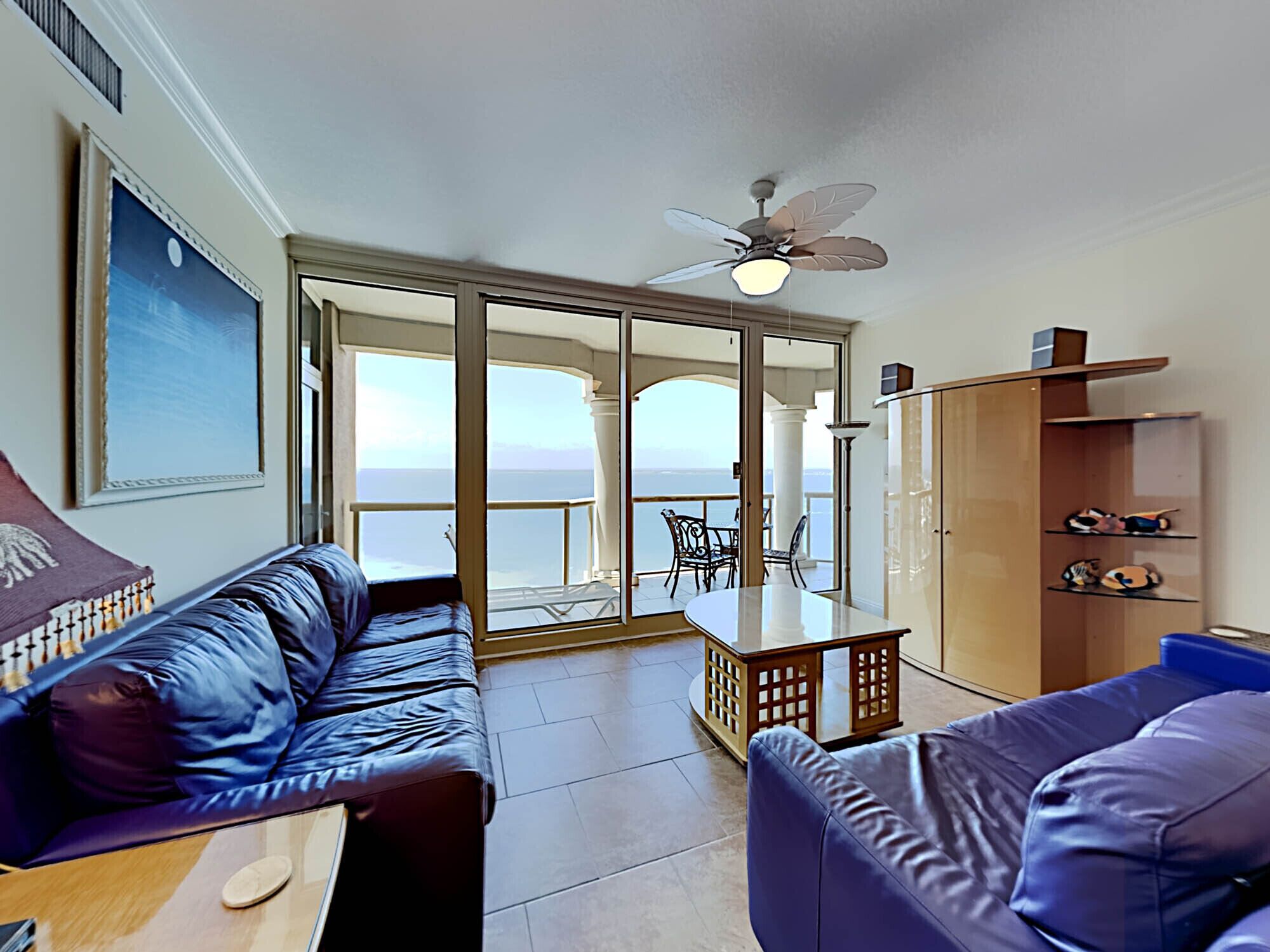 A living room with a sofa, a table, and a view of the sea through large glass doors.