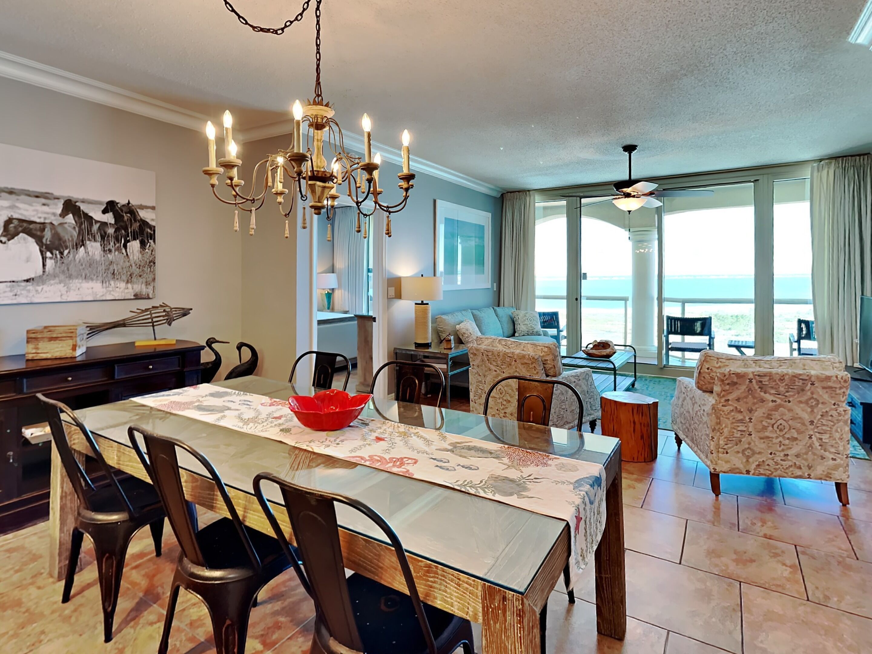 A spacious living area with a dining table, chairs, a chandelier, and a view of the ocean.