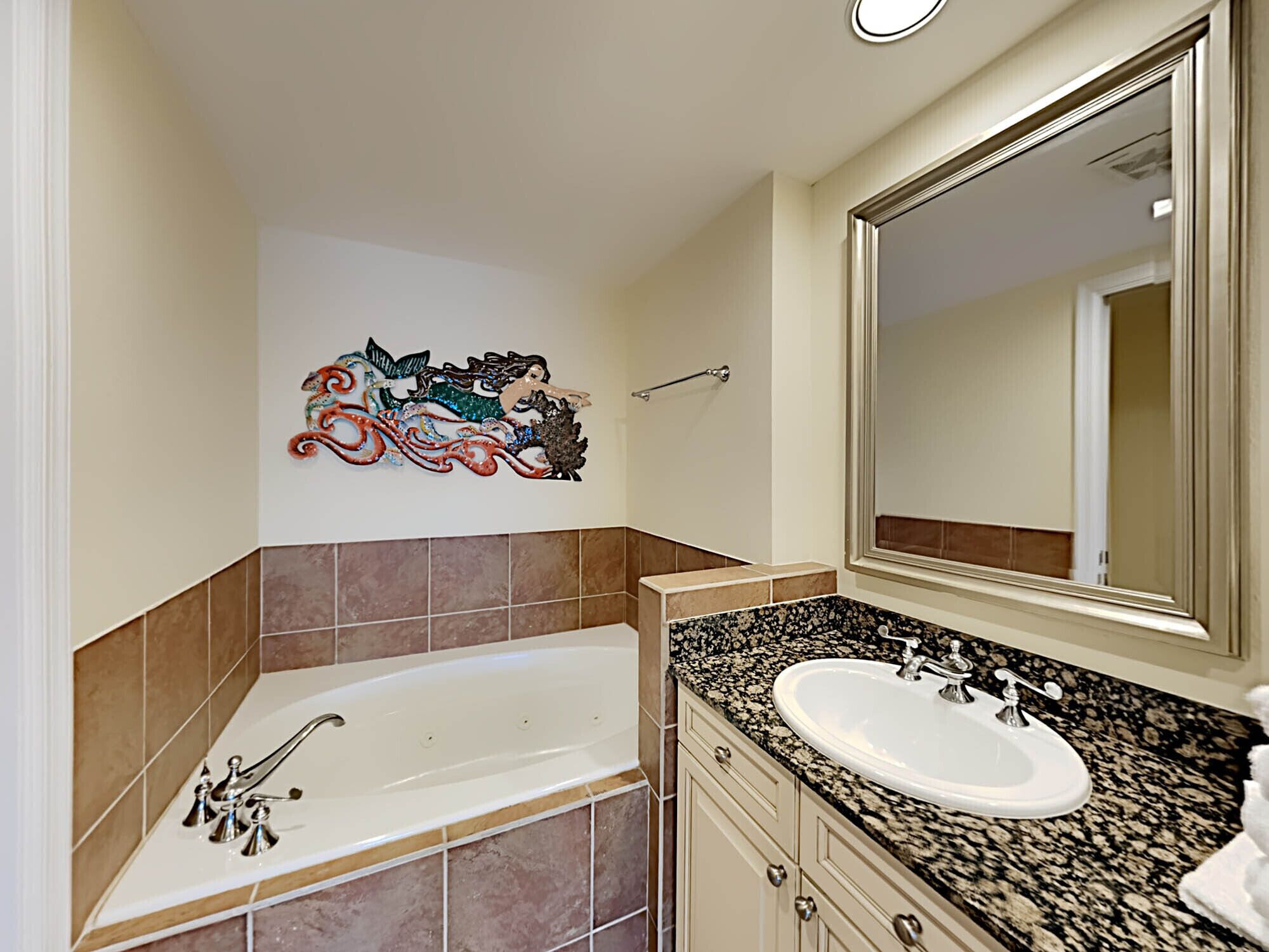 Een badkamer met een badkuip, een wastafel, een grote spiegel en een decoratief object aan de muur.