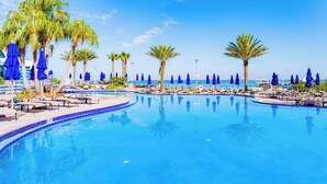 A pool area with lounge chairs and umbrellas, palm trees, and a clear view of the ocean.