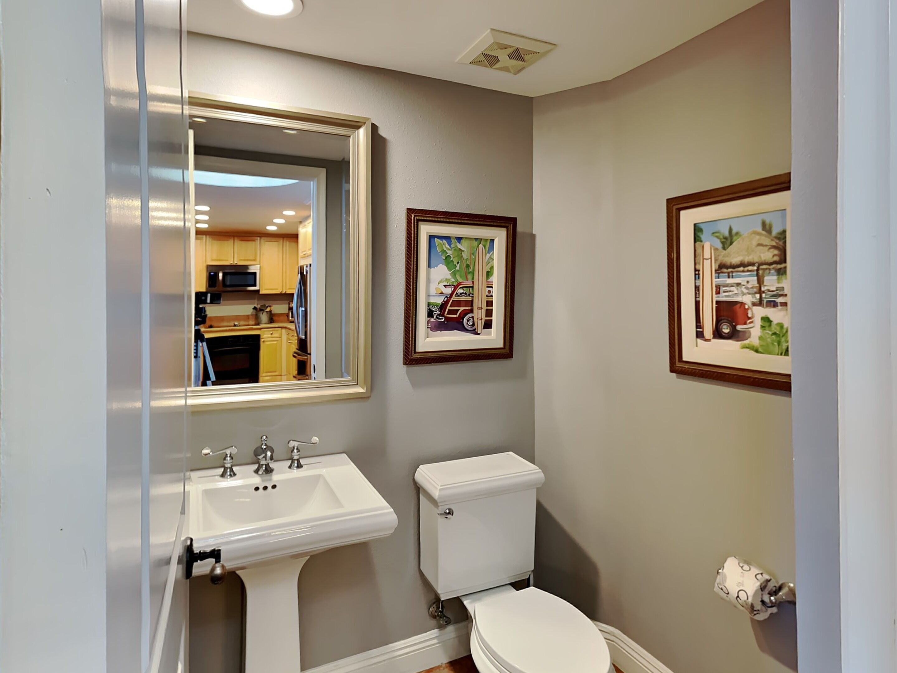 Een badkamer met een wit wastafelmeubel, toilet en een spiegel die uitkijkt over een keuken.