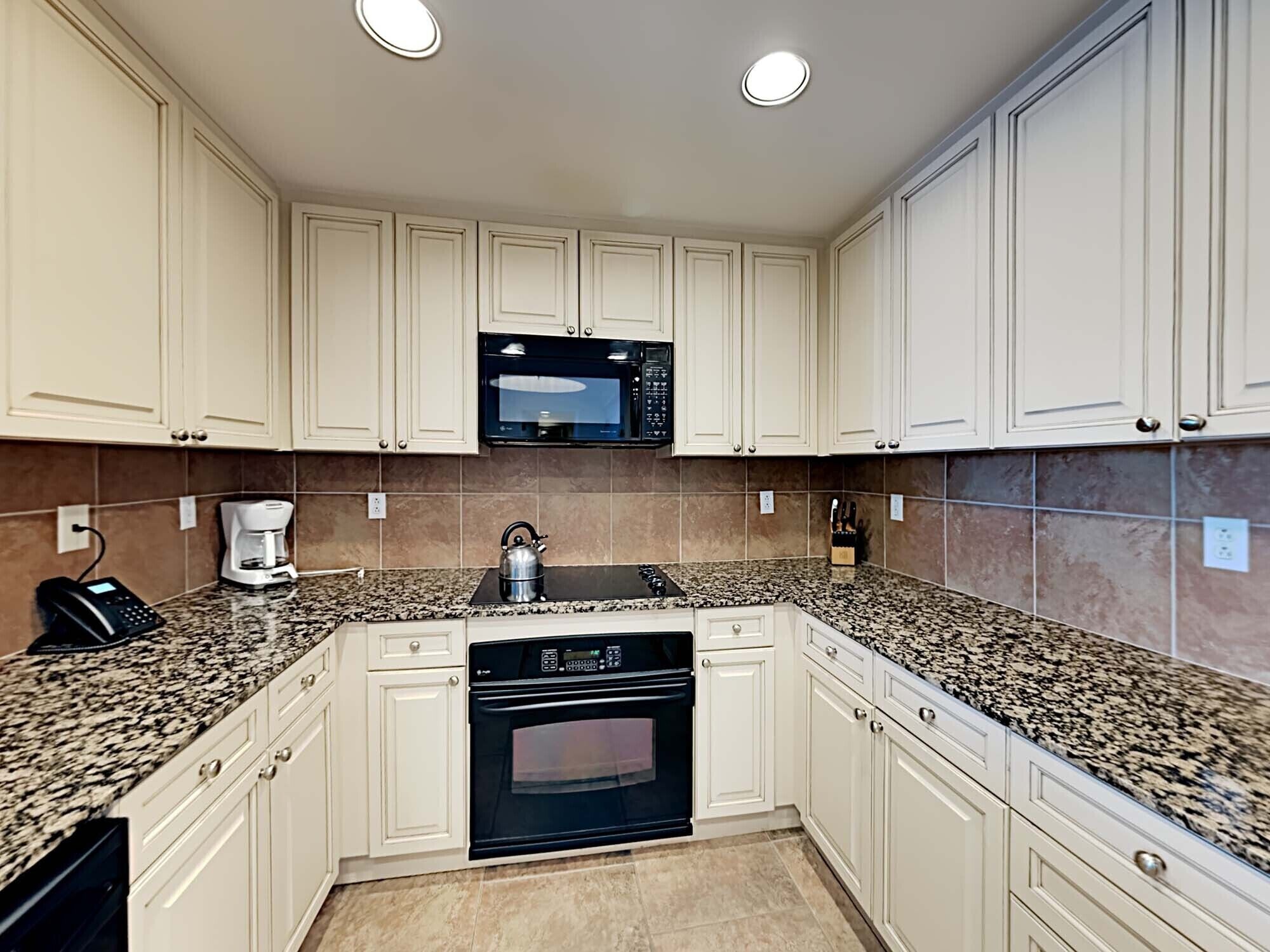 A kitchen with white cabinets, a microwave, a coffee maker, and a kettle on the counter.