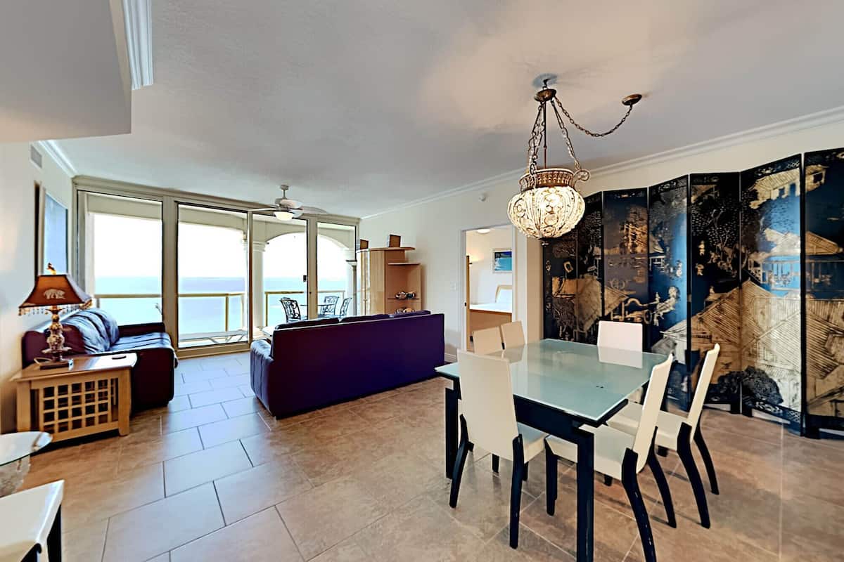 Een ruime woonkamer met een glazen eettafel, een bank en uitzicht op zee.