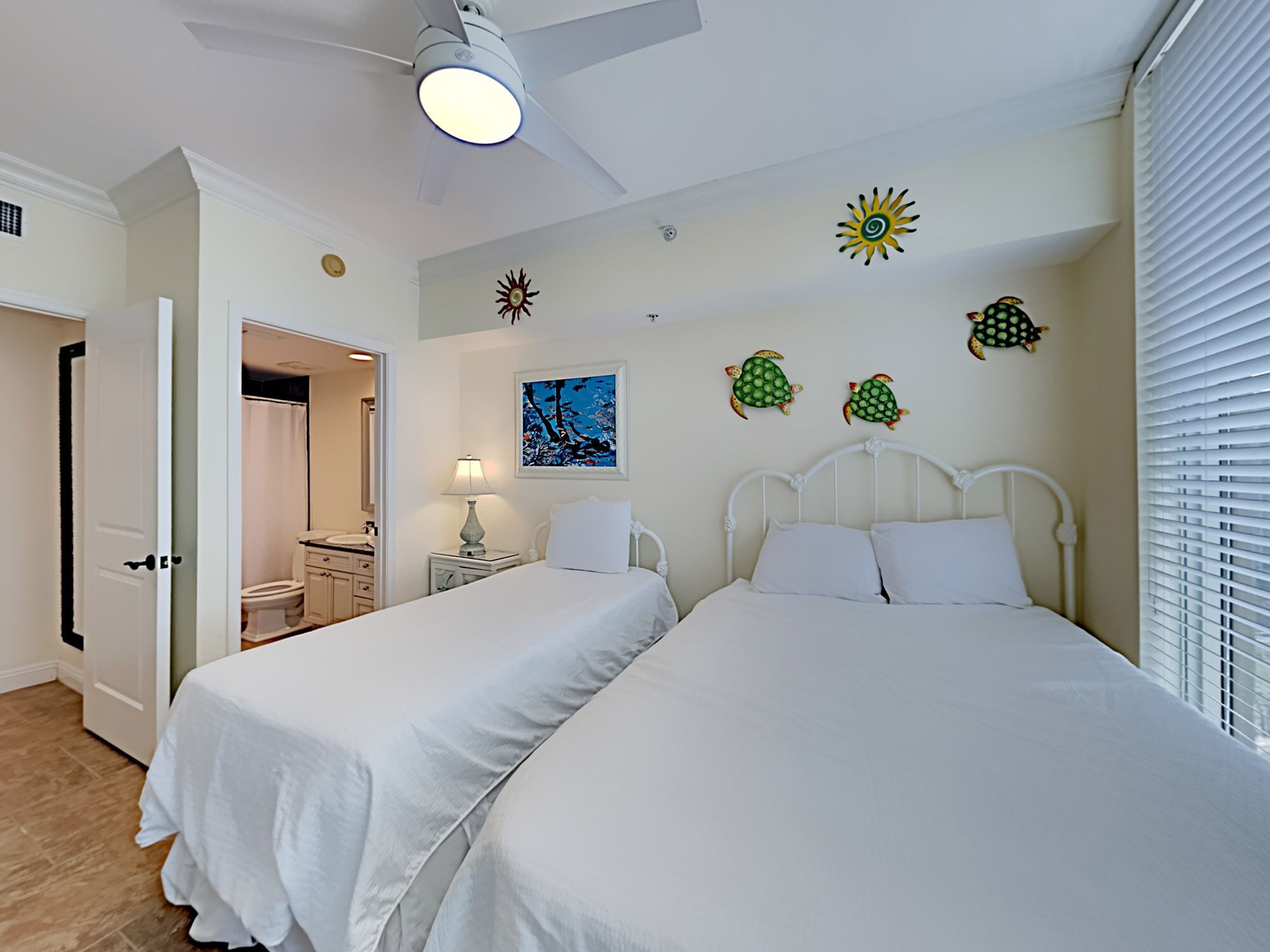 A bedroom with two beds, a ceiling fan, a nightstand with a lamp, and decorative wall art.