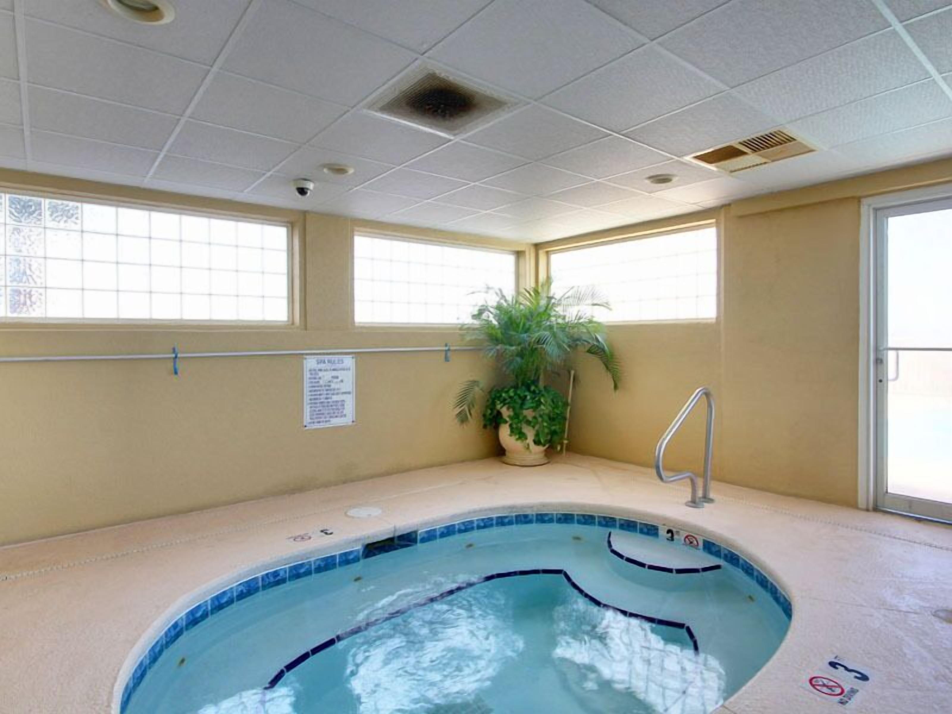 A small indoor pool with a blue tiled edge, a potted plant, and a sign on the wall.