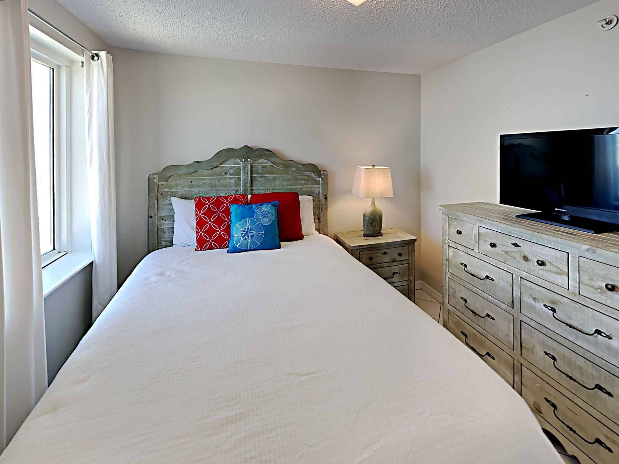 A bedroom with a bed, a dresser, a television, and a window with curtains.