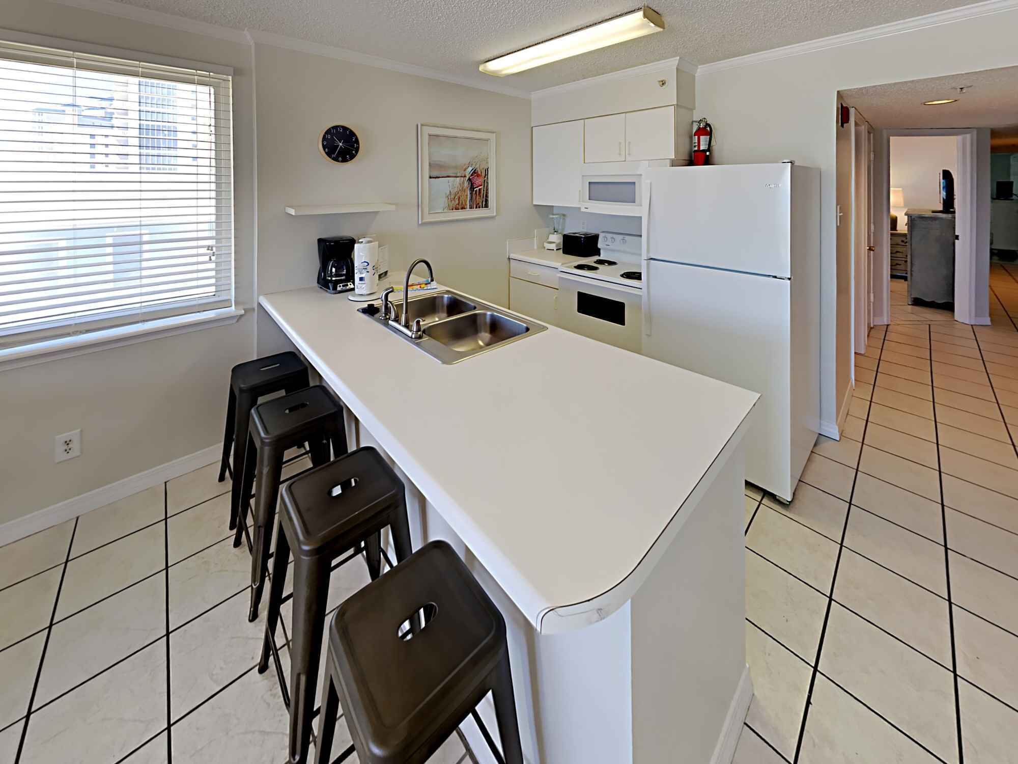 A modern kitchen with a central island, bar stools, a microwave, stove, and a refrigerator.