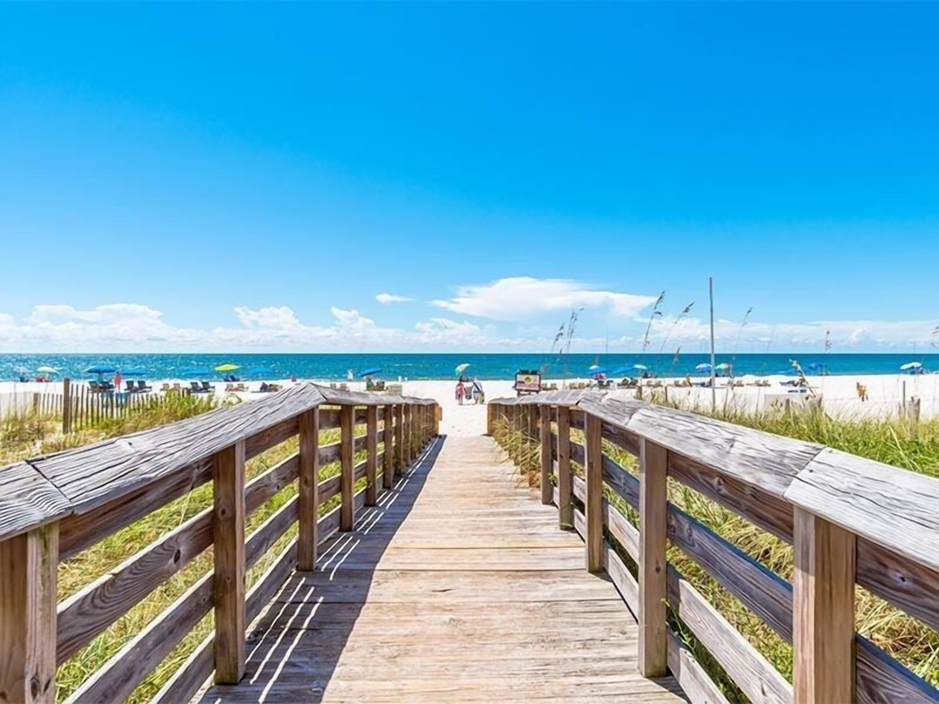 A wooden boardwalk leading to a beach with umbrellas and lounge chairs.