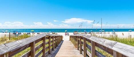 A wooden boardwalk leading to a beach with umbrellas and lounge chairs.