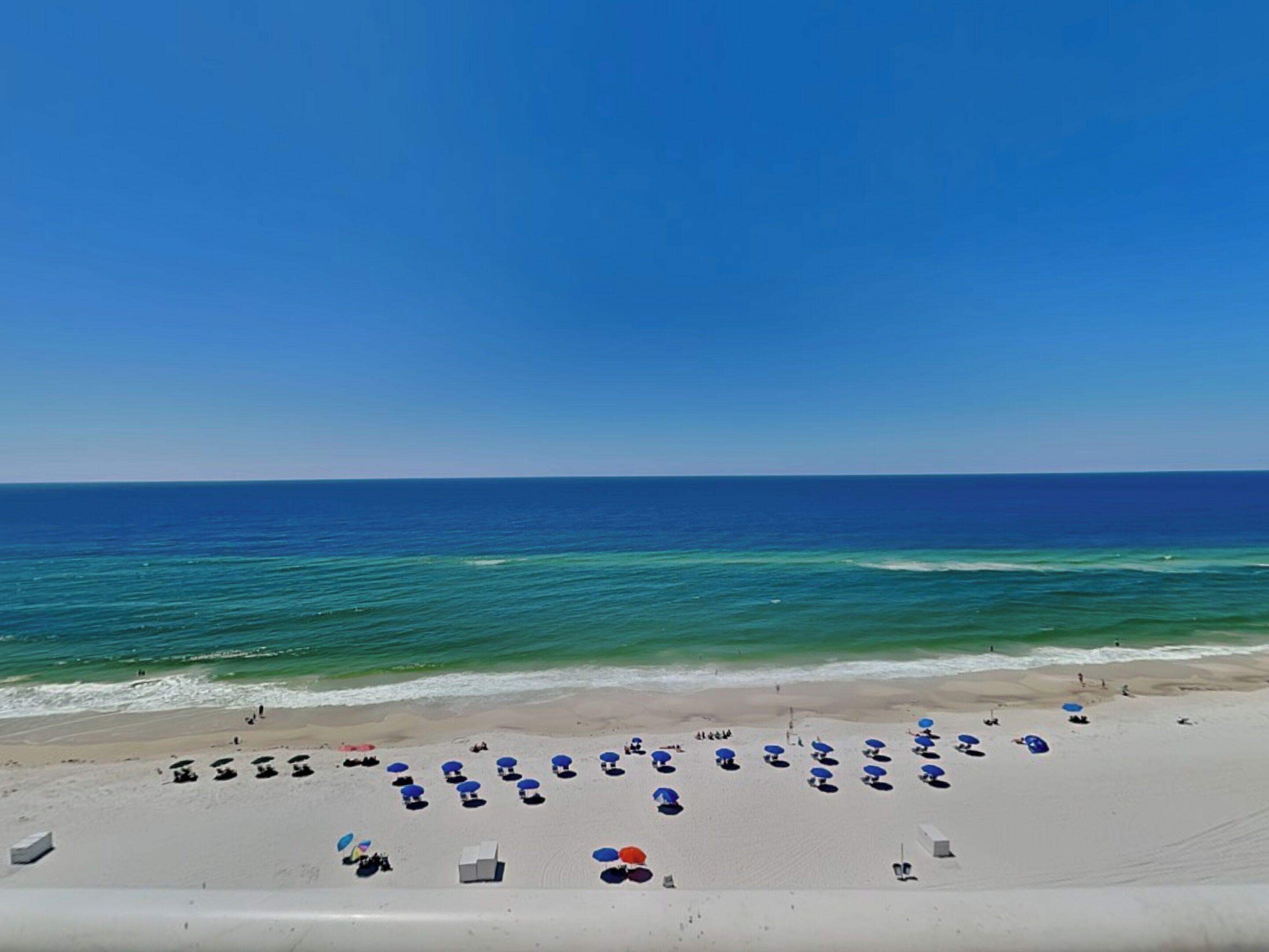 A beach with rows of umbrellas and lounge chairs, a clear sky, and the ocean.
