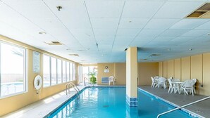 En inomhuspool med kristallklart blått vatten, omgiven av vita stolar och bord, och stora fönster på ena sidan.