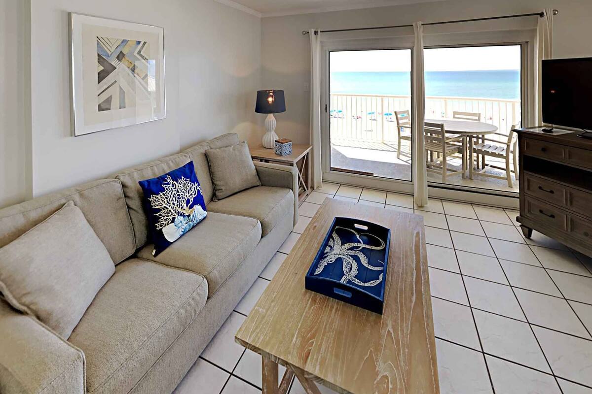 Un salón con sofá, una mesa de centro de madera, televisor y balcón con vista al mar.