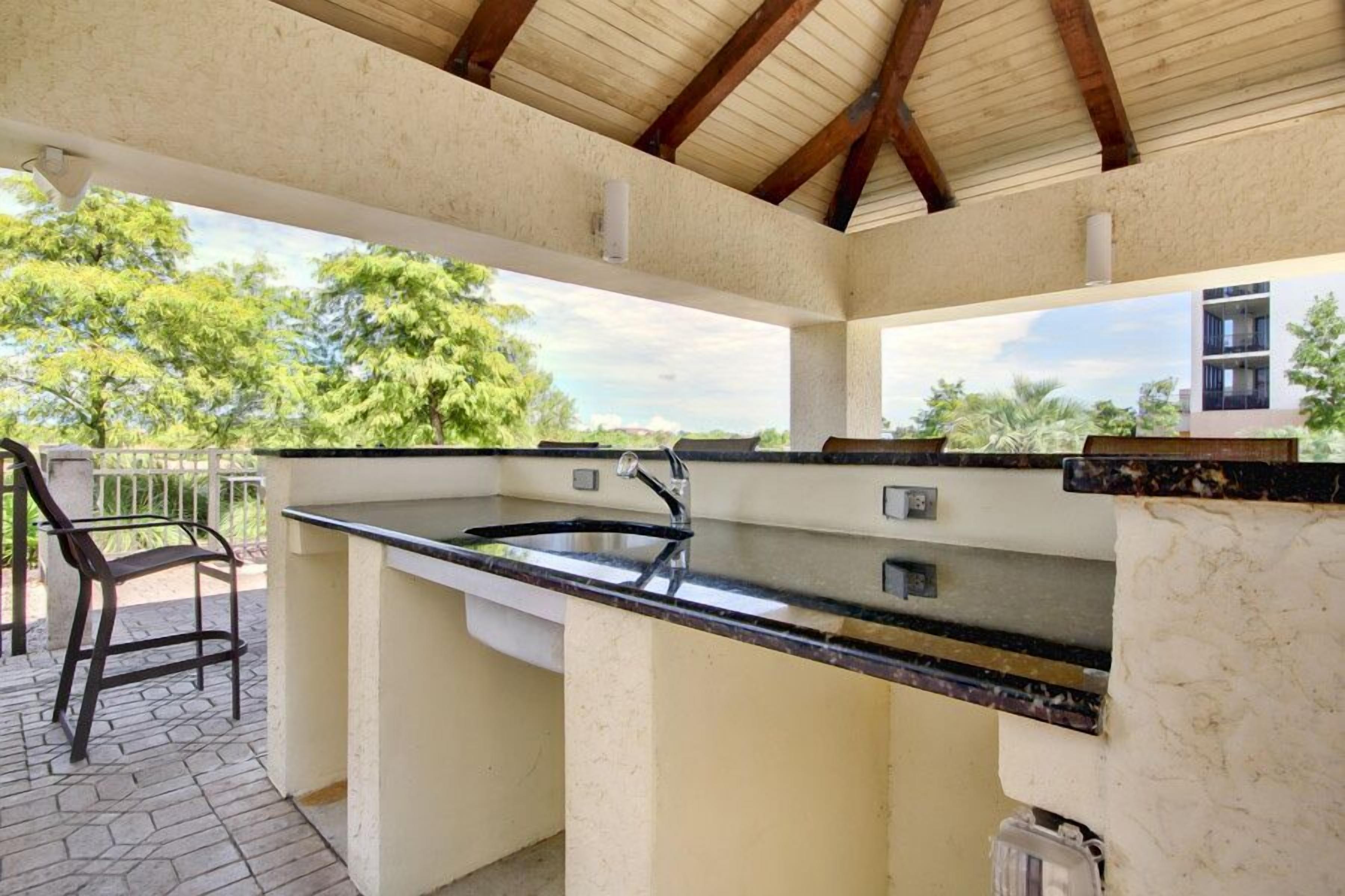 An outdoor kitchen with a sink and bar area, surrounded by a covered patio with a chair.