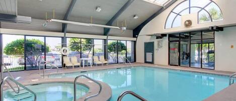 Una piscina interna con pareti di vetro trasparente, bordi curvi e un tetto apribile.