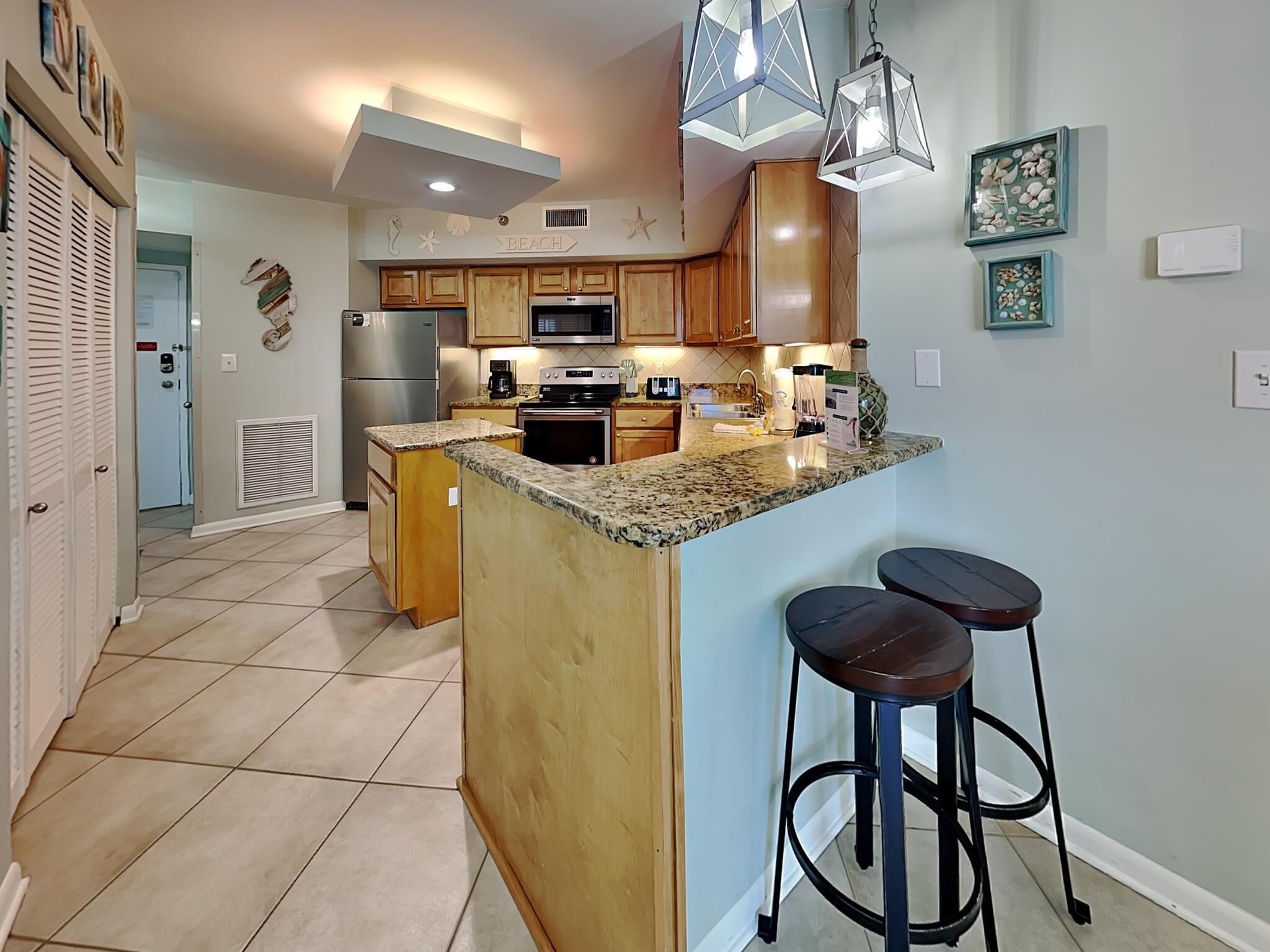 A modern kitchen with wooden cabinets, granite countertops, and a central island with bar stools.