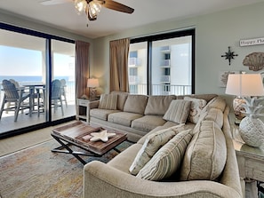 Relax in this inviting living area with a sofa set, wooden coffee table, and a rug, offering a scenic ocean view from the adjacent balcony.