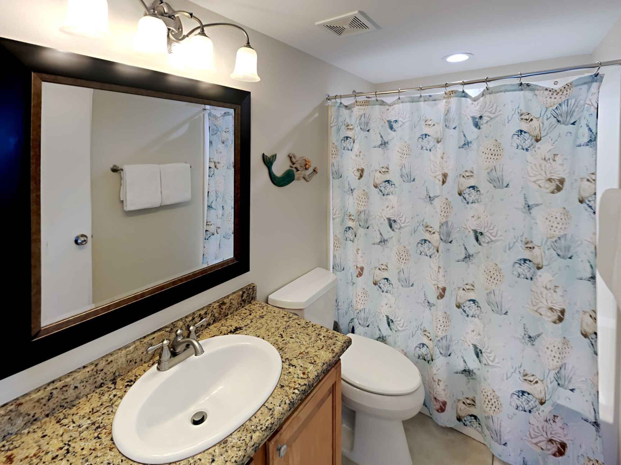A bathroom with a granite countertop sink, a white toilet, and a shower curtain with a sea life pattern.