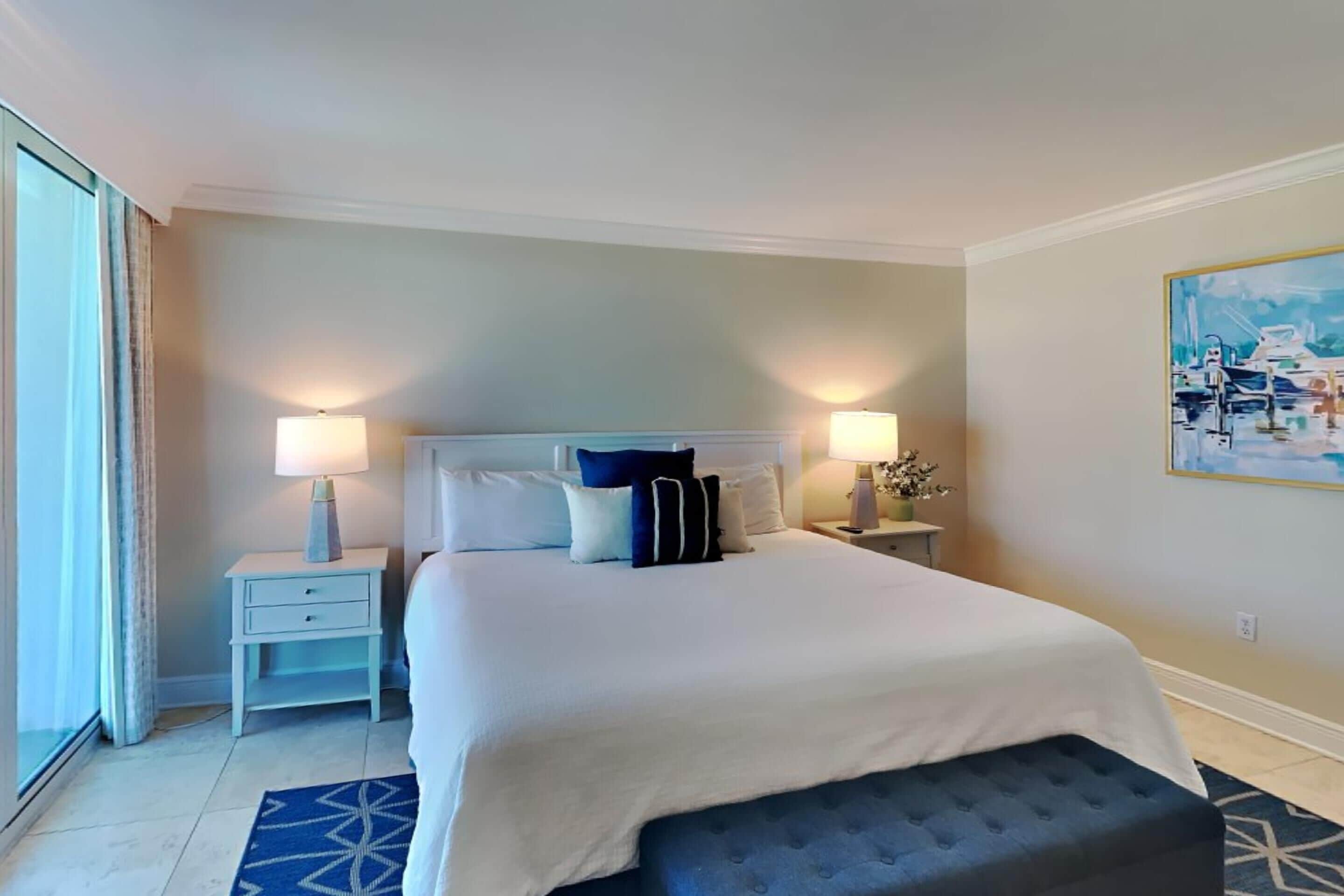 Een hotelkamer met een groot bed, twee nachtkastjes met lampen, een raam met gordijnen en een schilderij aan de muur.