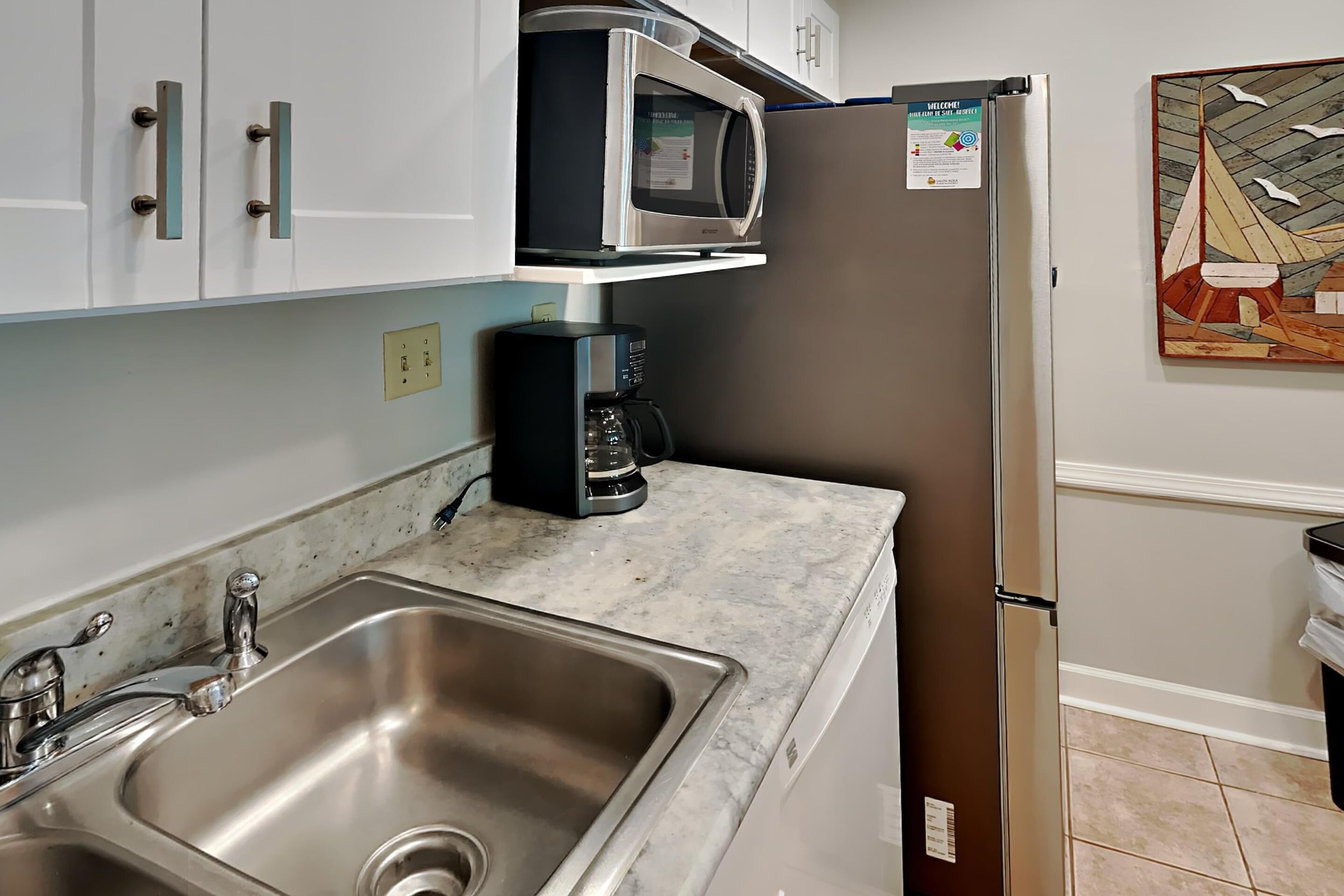 A kitchen with a stainless steel sink, a coffee maker, a microwave, and a refrigerator.