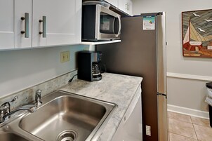 Una cocina con un lavamanos de acero inoxidable, una cafetera, un microondas y un refrigerador.