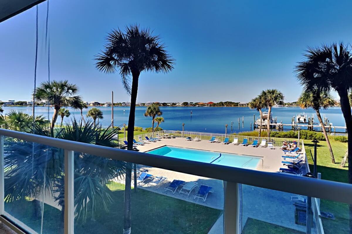 A pool area with lounge chairs and palm trees, overlooking a body of water.
