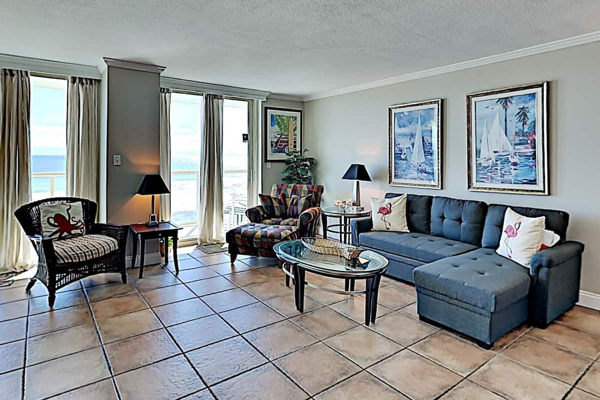 A living room with a sofa, armchairs, a coffee table, and a view of the ocean through large windows.