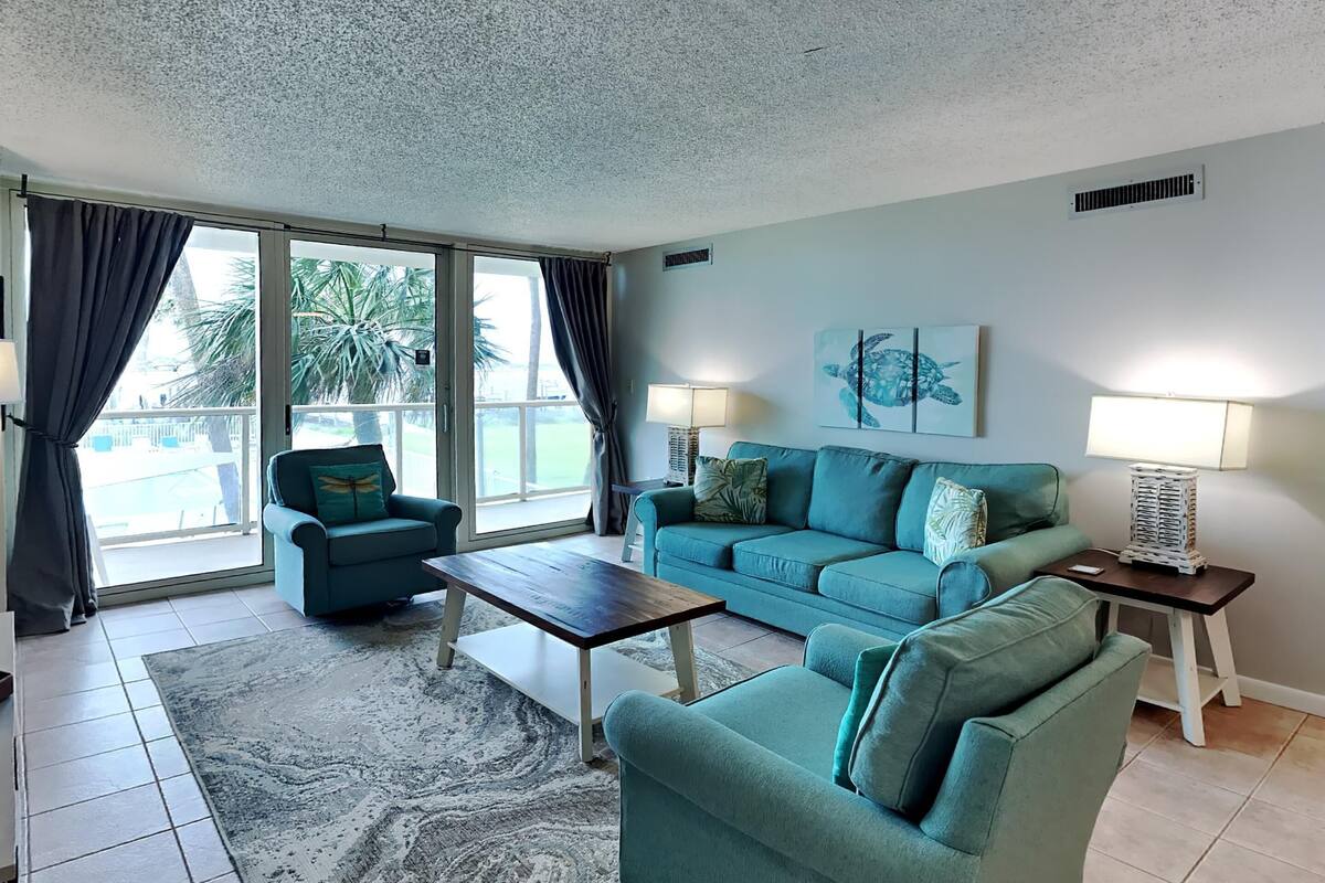 A living room with teal sofas, a wooden coffee table, and a large window with curtains.