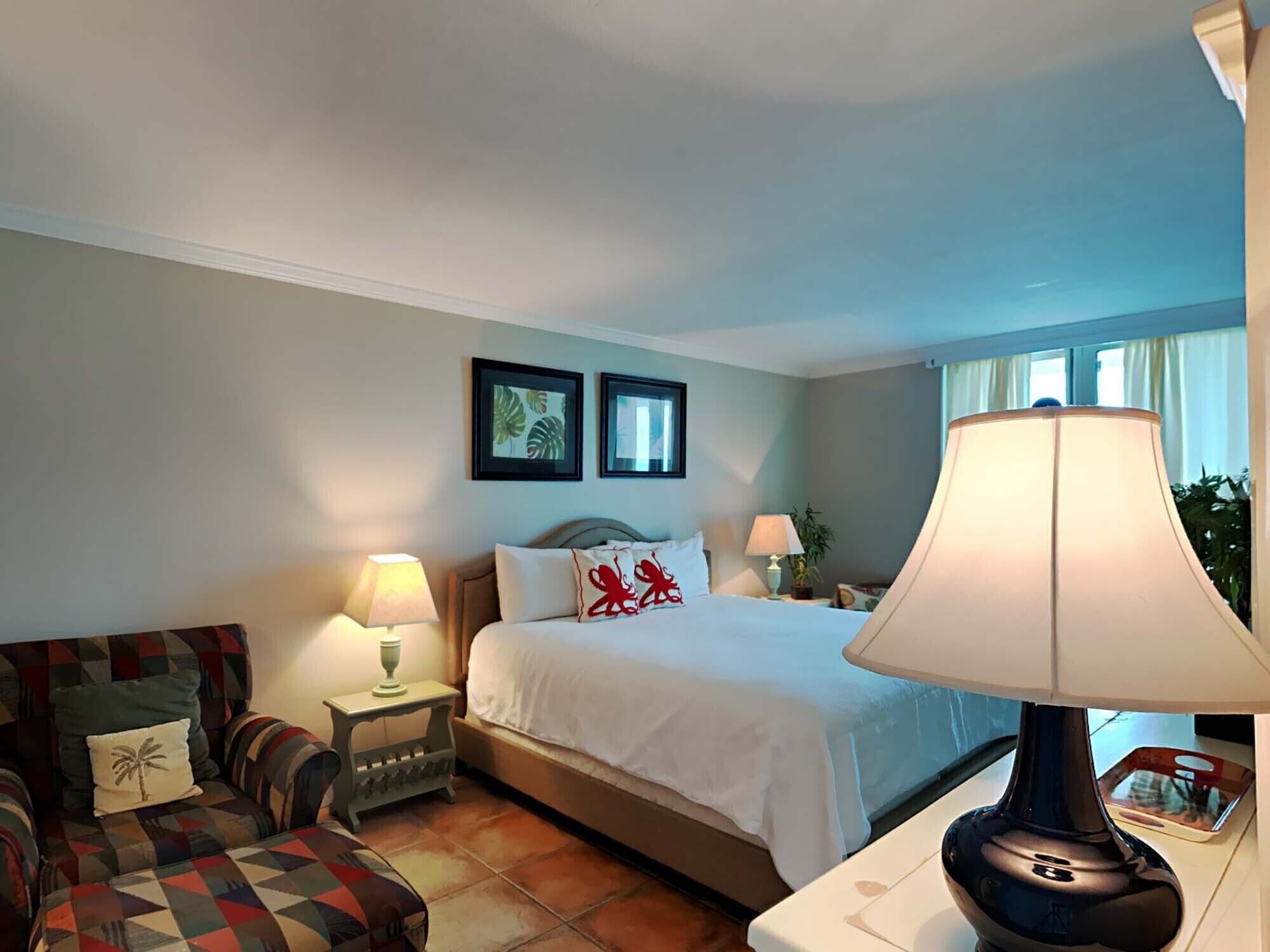 A hotel room with a bed, a sofa, a nightstand, a lamp, and two framed pictures on the wall.