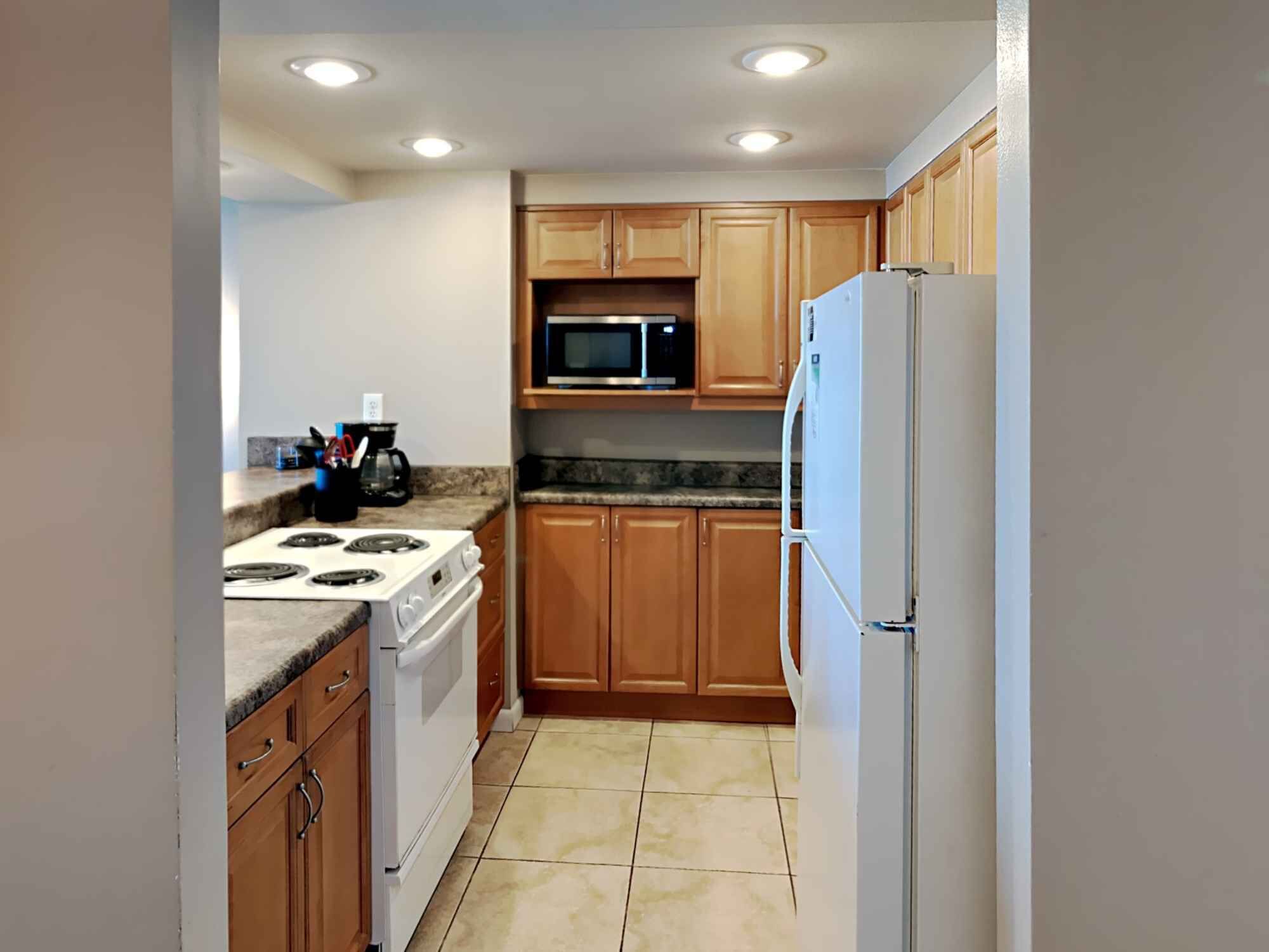 A compact kitchen with wooden cabinets, a white stove, a microwave, and a refrigerator.