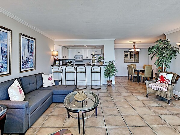 A living room with a sofa, a glass coffee table, and a dining area with chairs and a table. - Sabine Yacht & Racquet by Southern Vacation Rentals (Pensacola Beach)