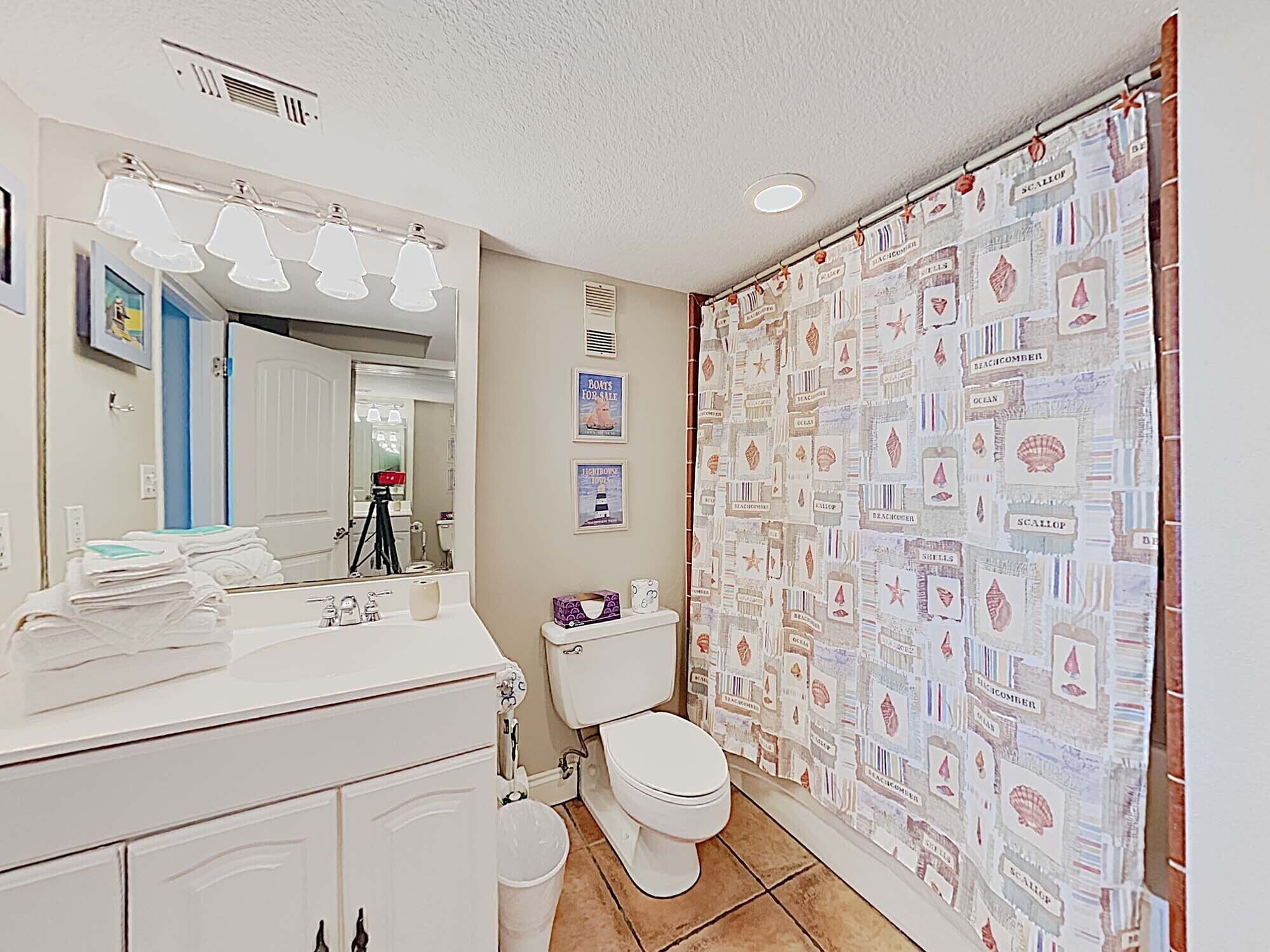 Une salle de bain équipée de toilettes, d’un lavabo et d’un miroir. On y trouve un rideau de douche orné de motifs sur le thème de la marine.